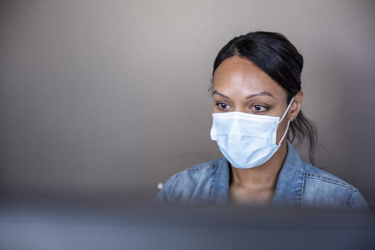 Woman wearing a mask sitting behind a computer monitor at the UW Belltown COVID-19 Clinic. Credit: University of Washington