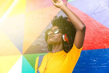 Women standing in front of colorful background wearing headphones with fist raised
