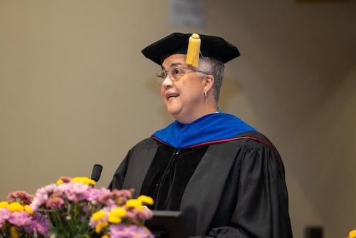 DGH Chair Heidi van Rooyen stands behind a podium and addresses the crowd during graduation.